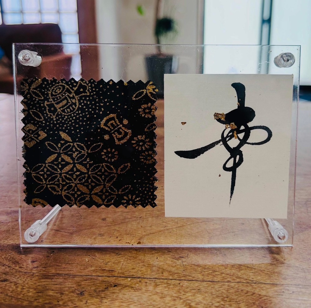 作品の見本。アクリルの額の左に金彩の布、右に「夢」の一文字。